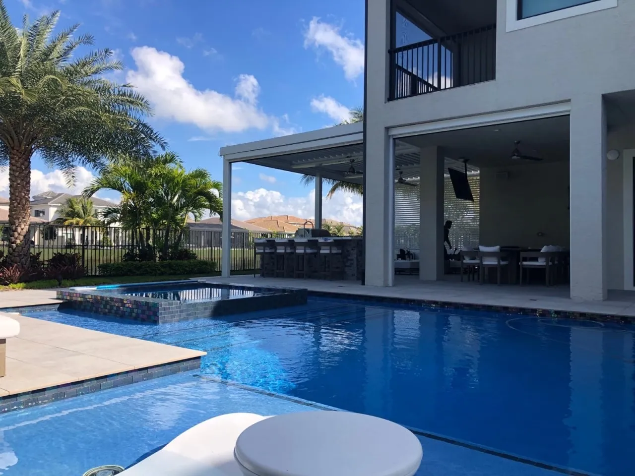 Pool with raised glass-tile spa in front of a louvered pergola and outdoor bar.