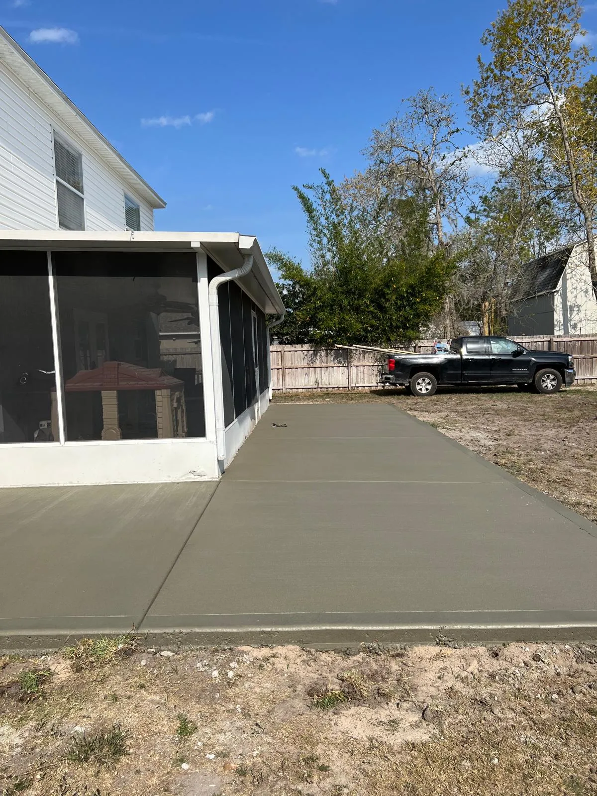 New concrete patio slab extending along a white screen room on a two-story house.