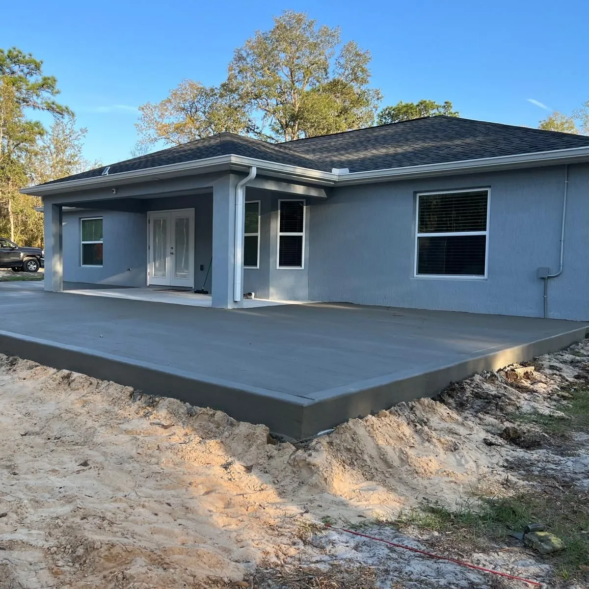 Raised concrete patio slab wrapping the back porch of a new blue-gray stucco house.