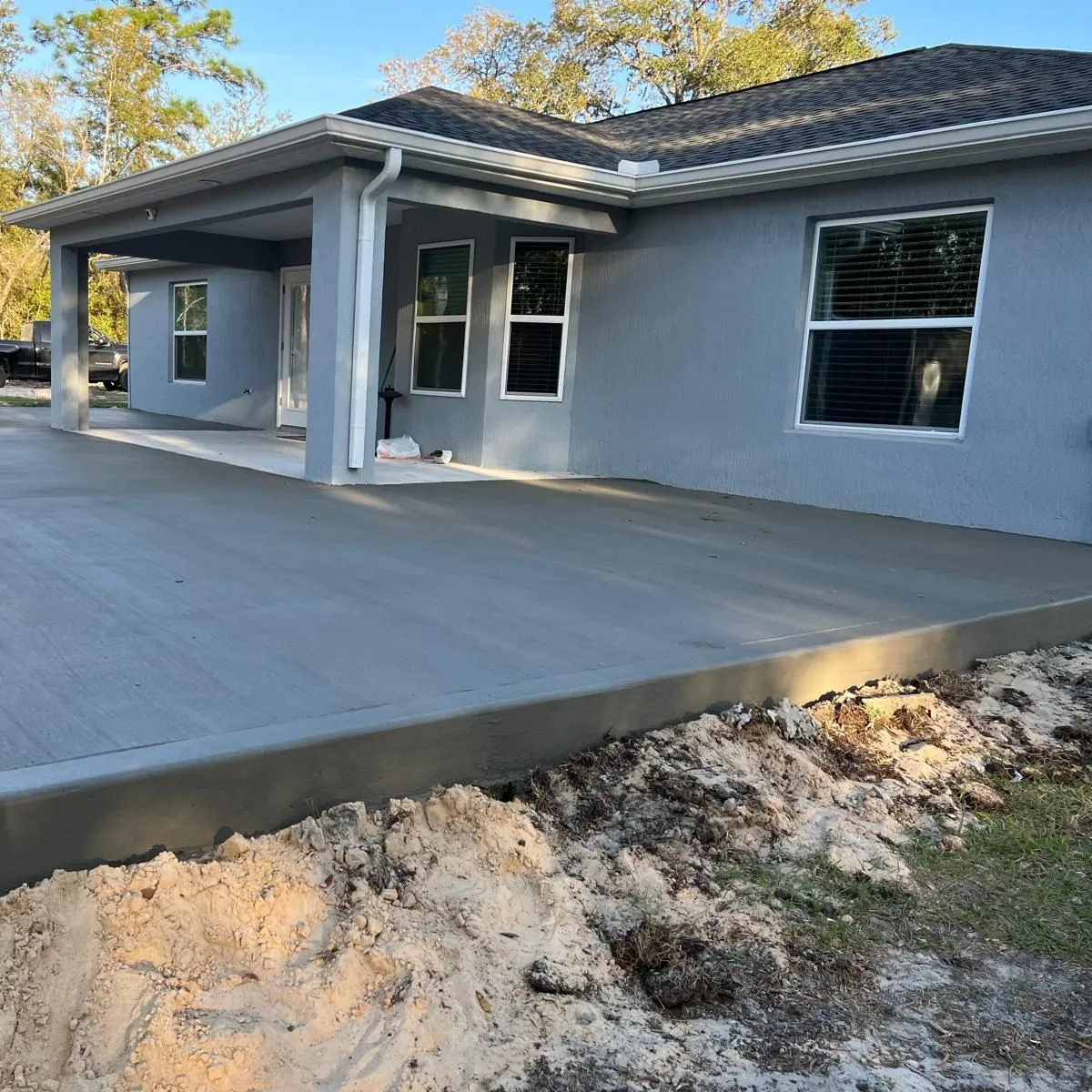 Corner view of a raised broom-finished concrete patio slab beside a blue-gray stucco house.