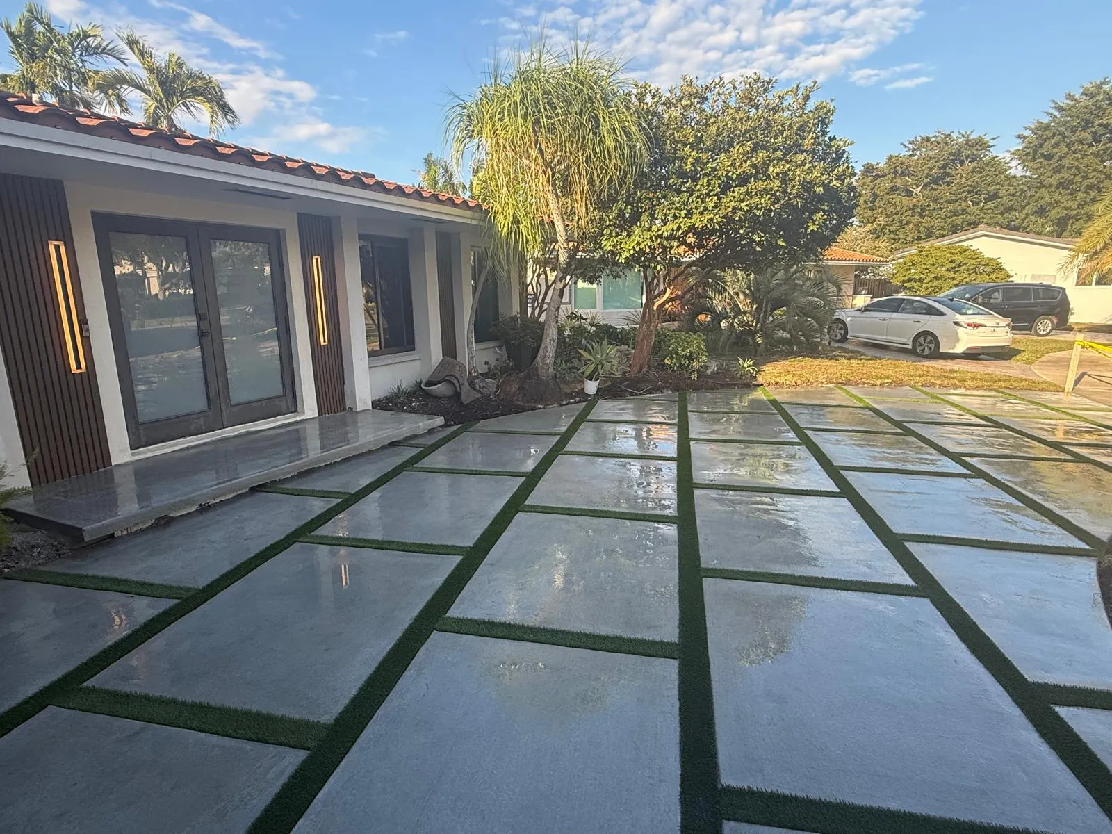 Large concrete slab driveway with artificial turf joints in front of a modern entry with LED sconces.