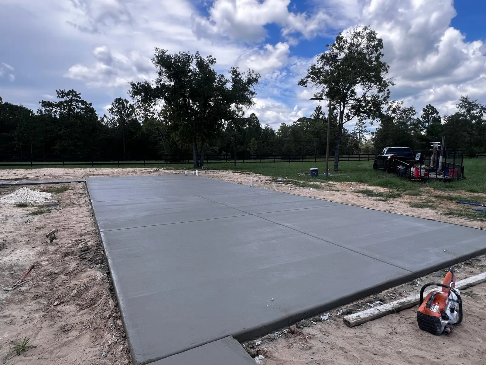 Large rectangular concrete slab with control joints on a rural lot with black fence.
