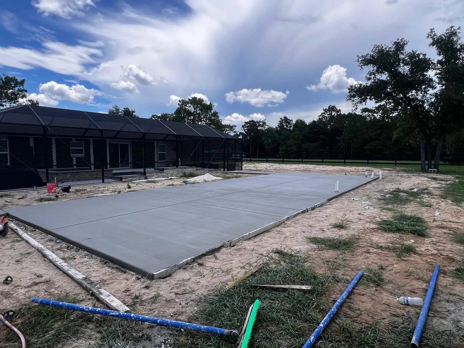 New concrete slab beside a black screen pool enclosure under a dramatic sky.
