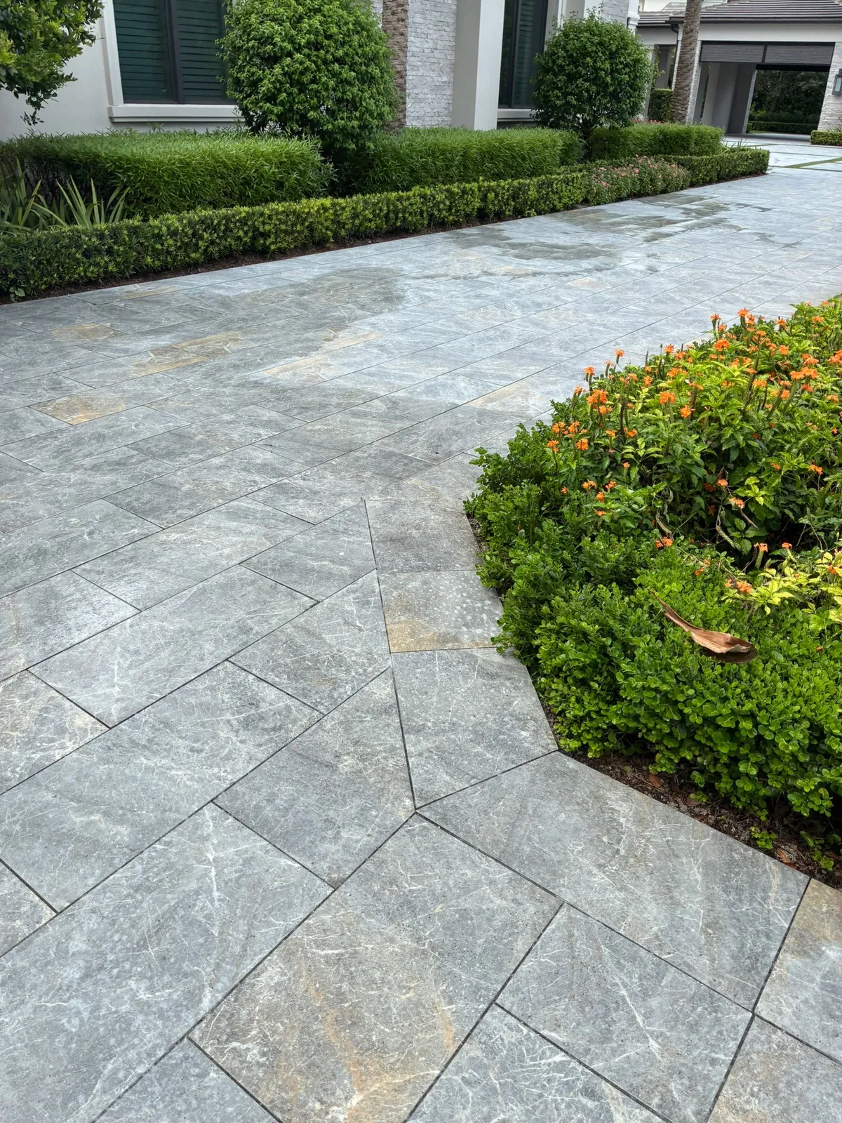 Gray marble pavers with an angled inlay along boxwood hedges and orange flowers.
