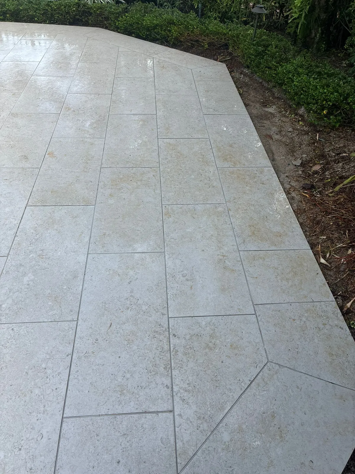 Large-format cream limestone pavers with a mitered angled border along a hedge.