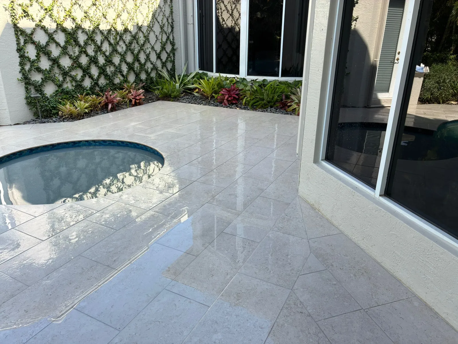 Wet limestone pool deck around a round spa with a vine trellis wall and bromeliads.