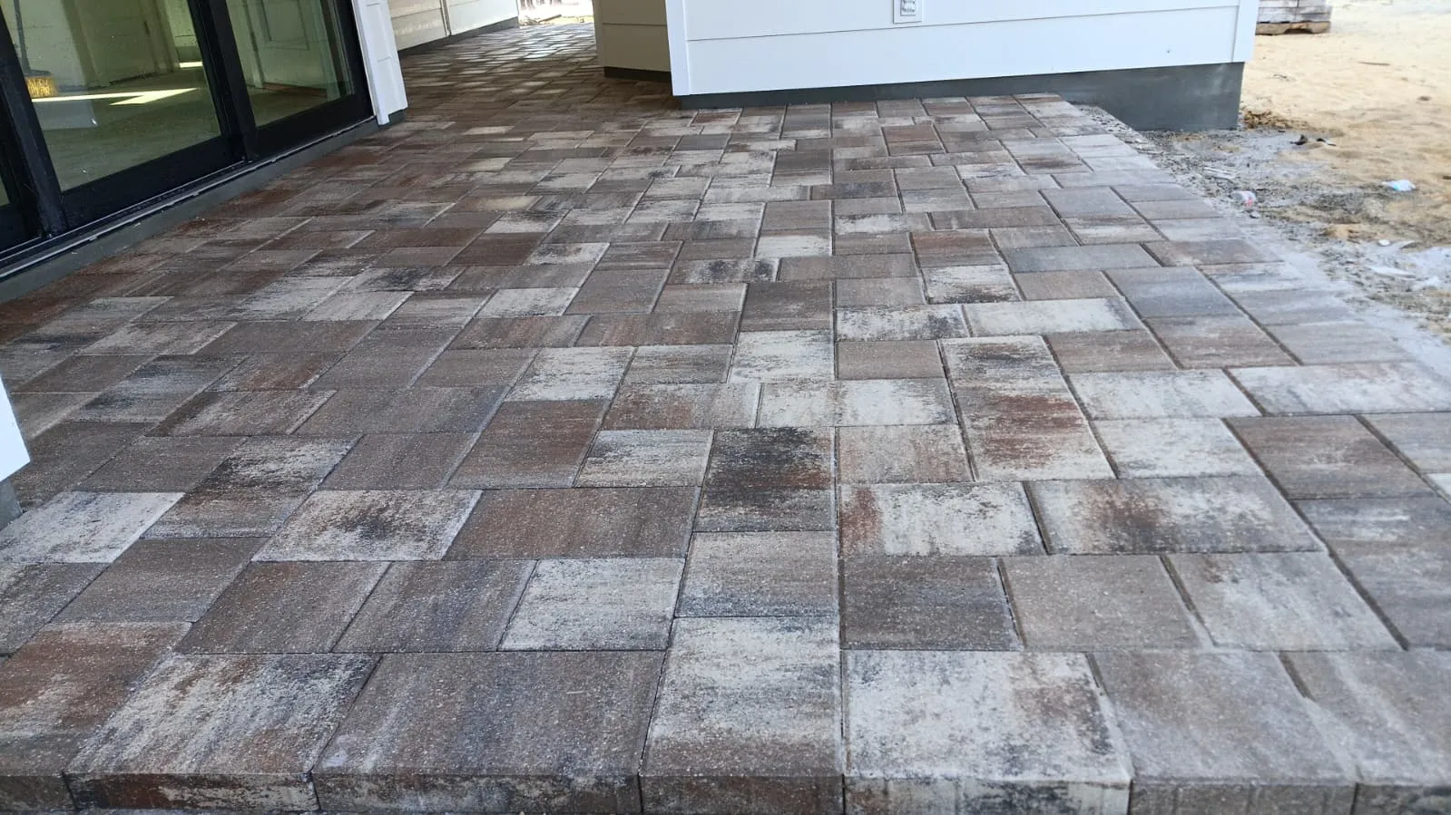 Brown and cream blend concrete paver patio outside sliding doors of a new white house.