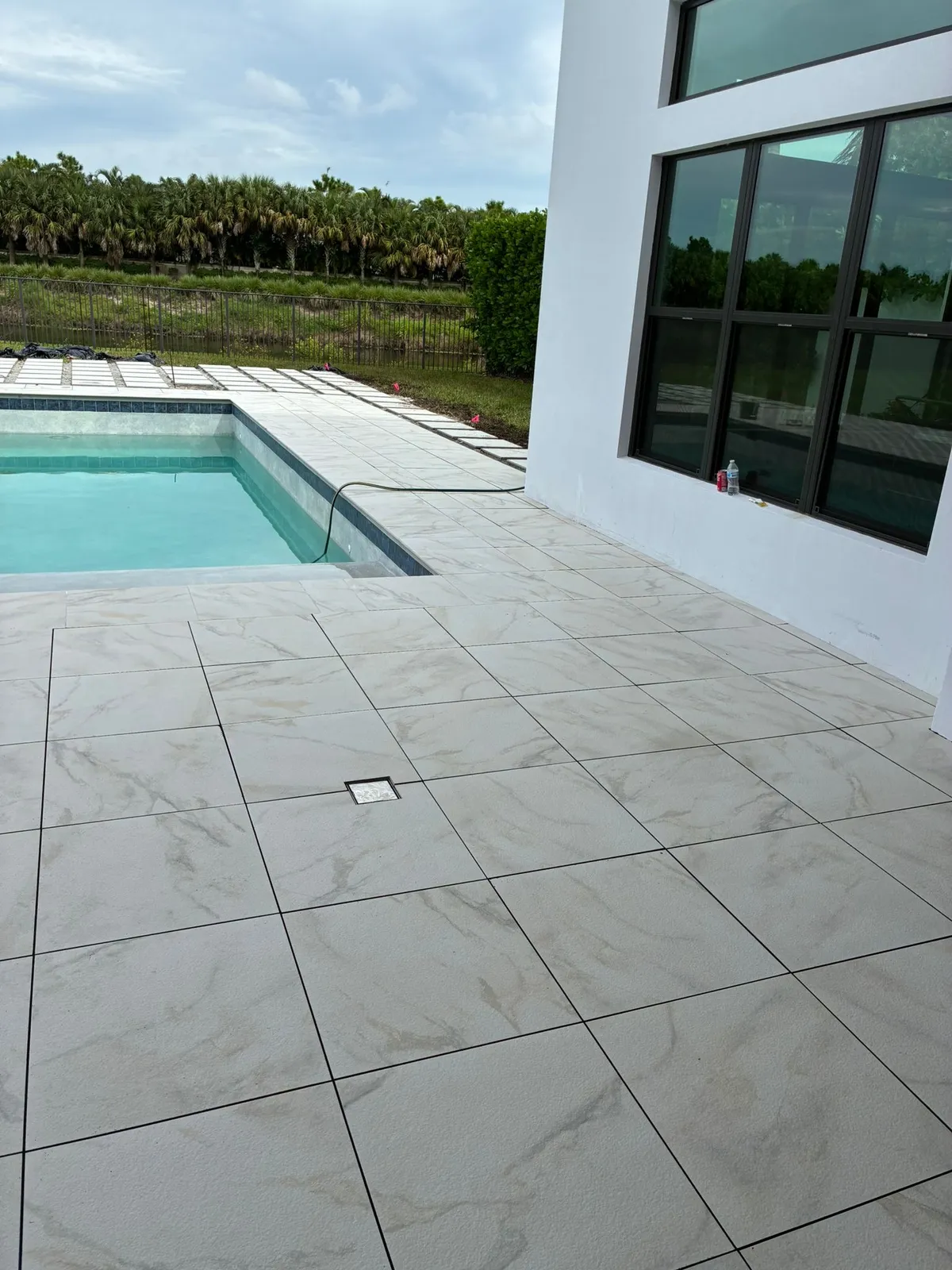 Large-format marble-look porcelain pavers on a pool deck beside a turquoise pool.