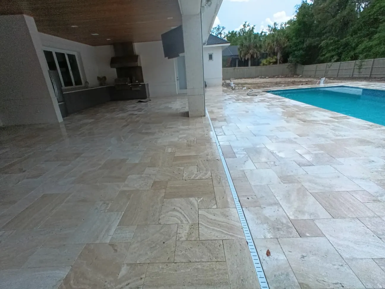 Travertine paving running from a covered patio to the pool deck with a linear drain.