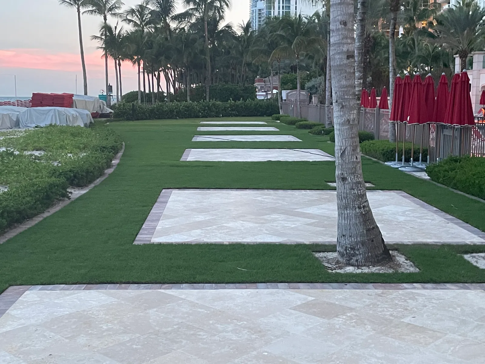Row of travertine pads with paver borders set in a resort lawn at sunset.