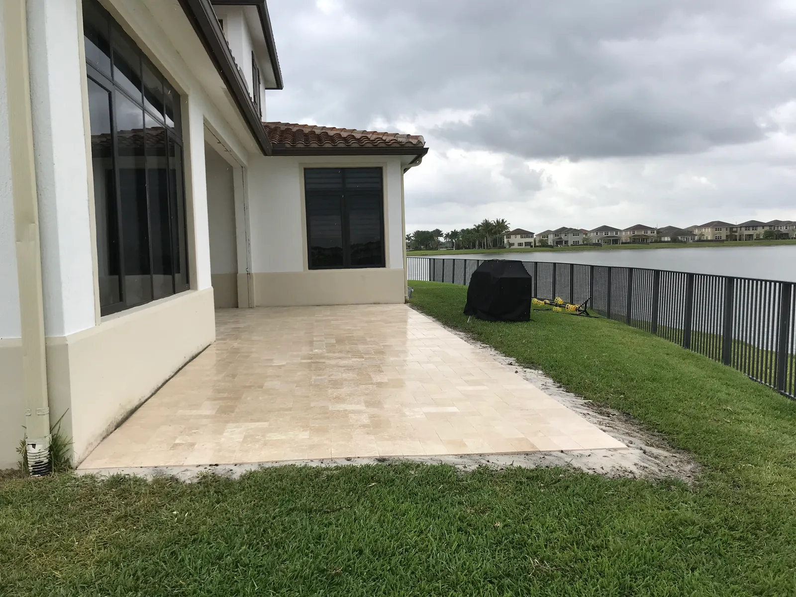 Ivory travertine paver patio behind a stucco house with a lake and storm clouds.