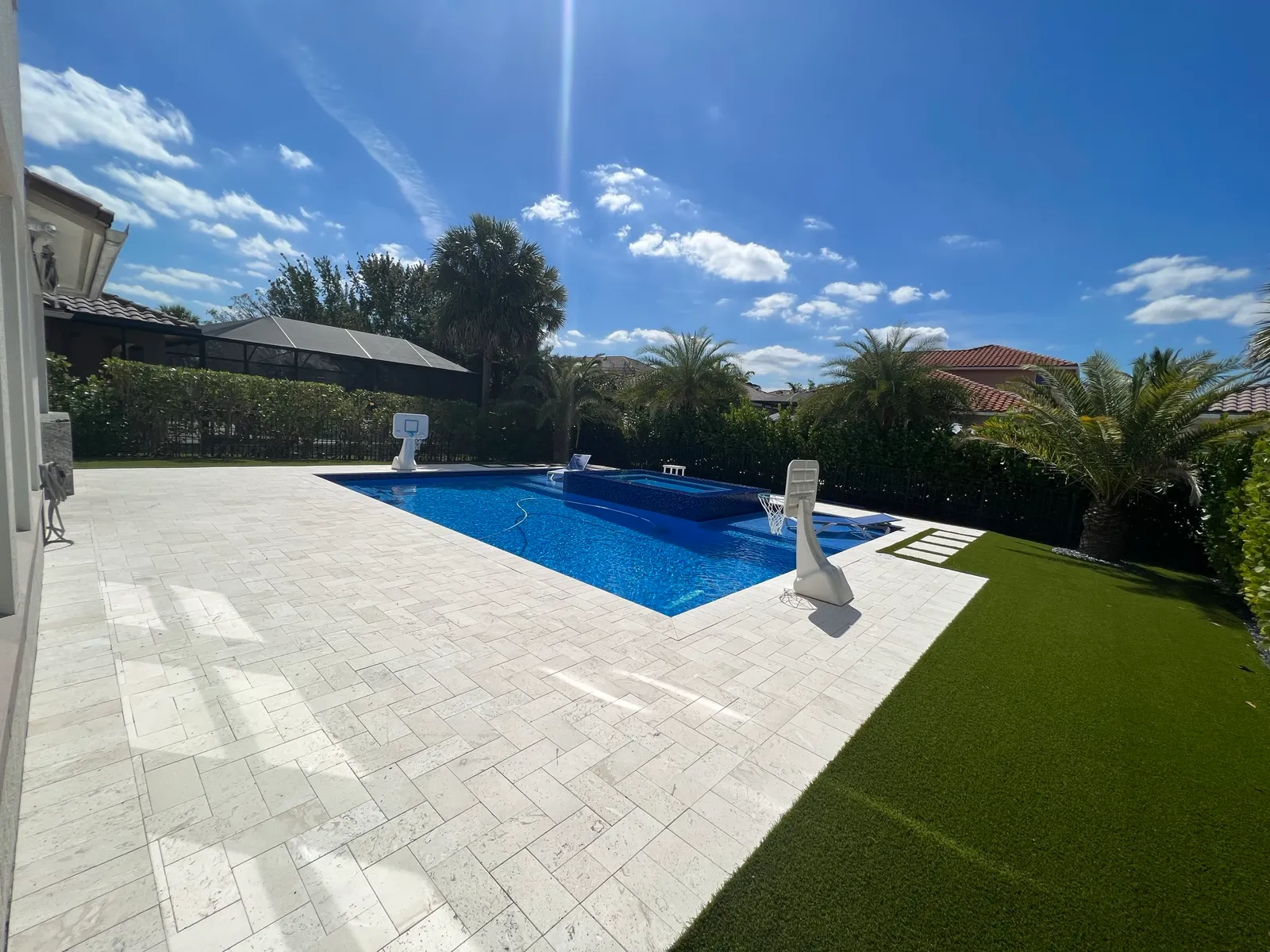 Ivory travertine pool deck laid in a herringbone pattern with artificial turf border and pool beyond.