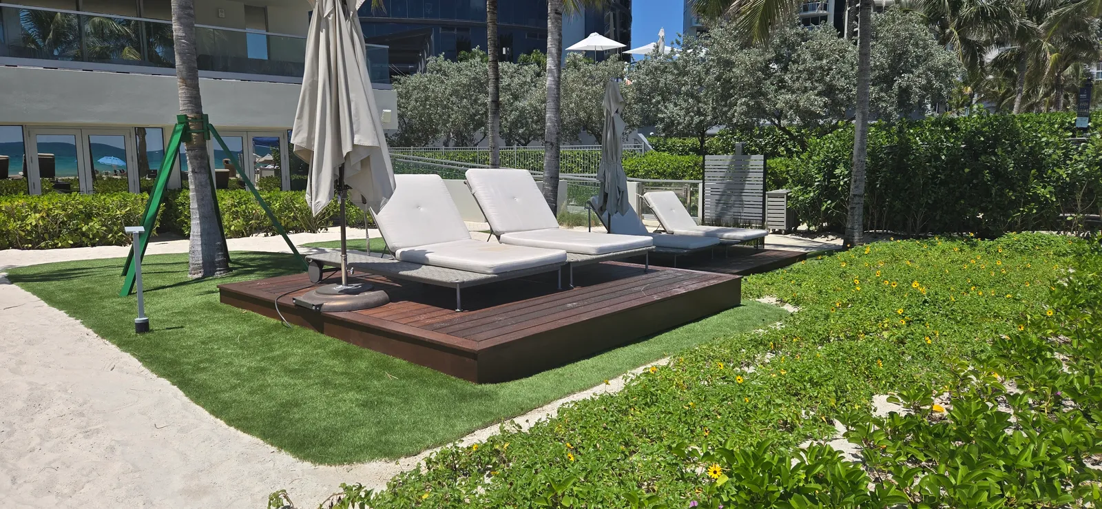 Dark hardwood lounge deck with daybeds set on artificial turf beside dune planting.