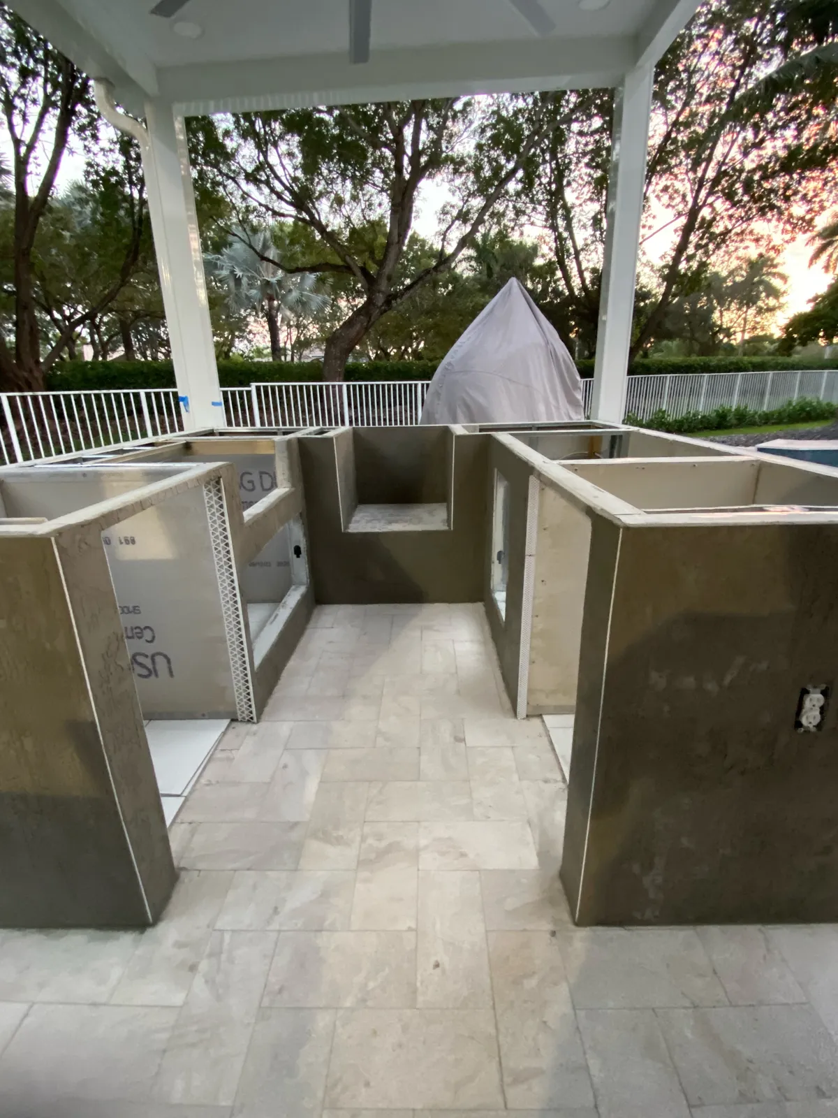 U-shaped outdoor kitchen base with cement board and scratch coat under a white pavilion.