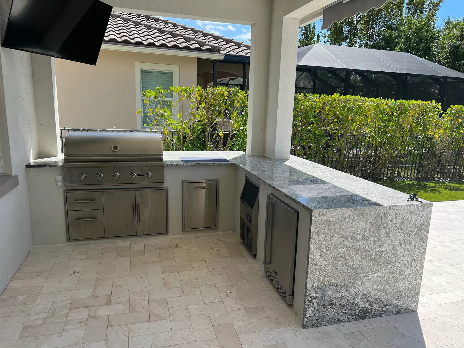 Outdoor kitchen with granite waterfall countertop, built-in grill and undercounter fridge on a stone patio.