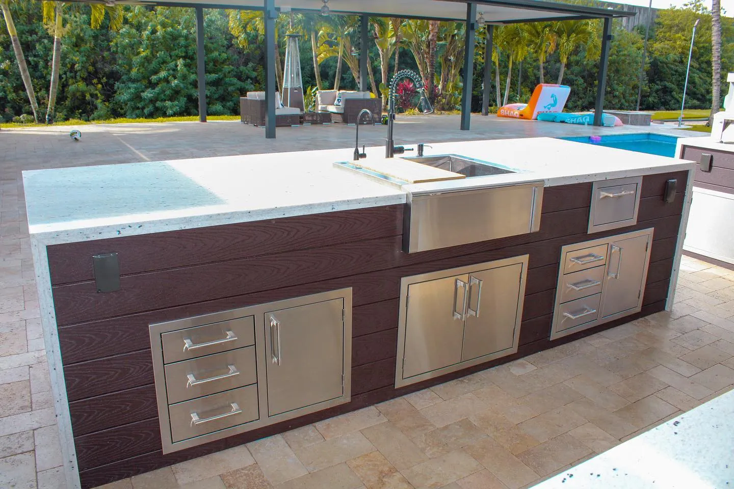 Outdoor kitchen island with stainless farmhouse sink and drawers on brown composite cladding.