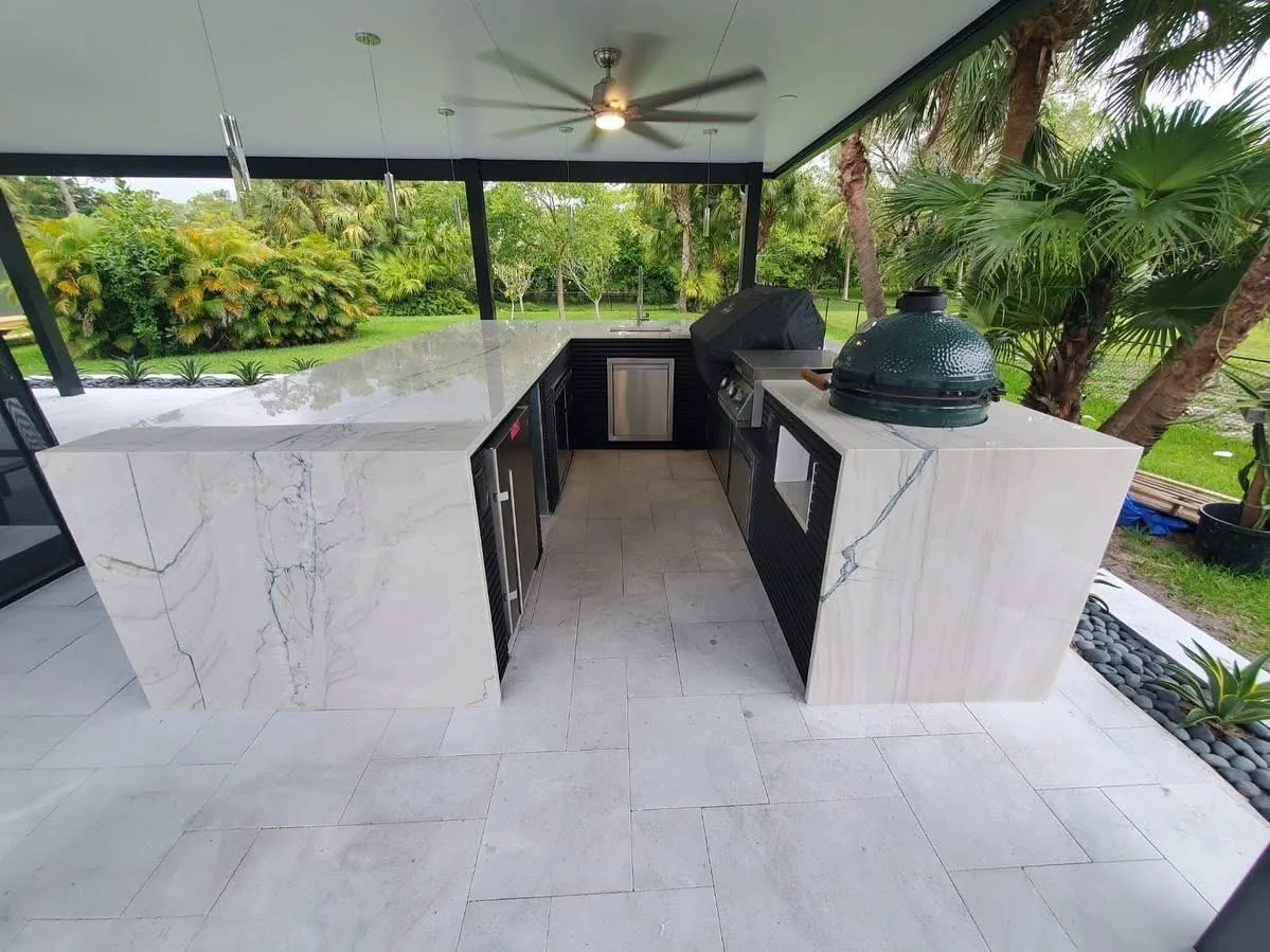 U-shaped outdoor kitchen with marble waterfall counters and a kamado grill under a patio cover.