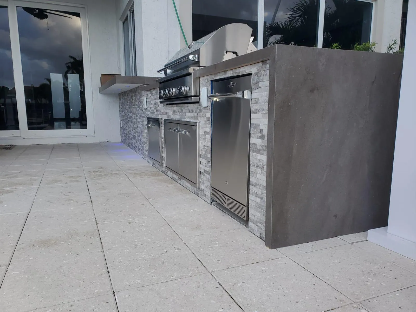 Outdoor kitchen with gray stacked stone, concrete-look waterfall end and built-in grill.