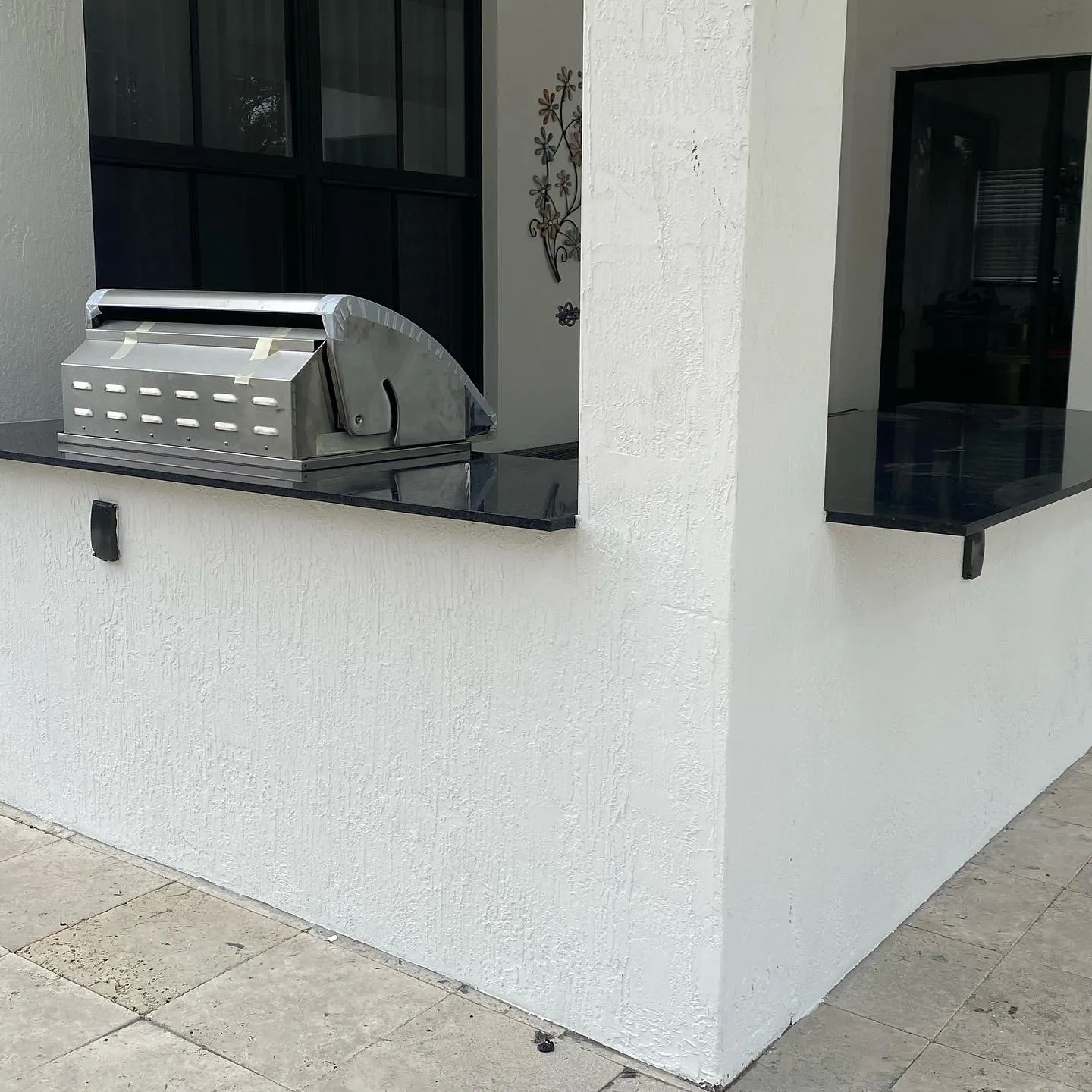 White stucco outdoor kitchen with black granite countertop and a built-in grill still wrapped.