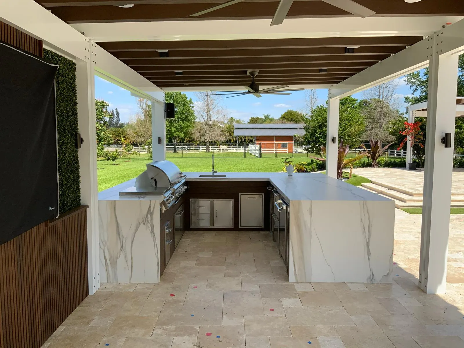 U-shaped outdoor kitchen with marble-look waterfall counters under a white and wood pergola.