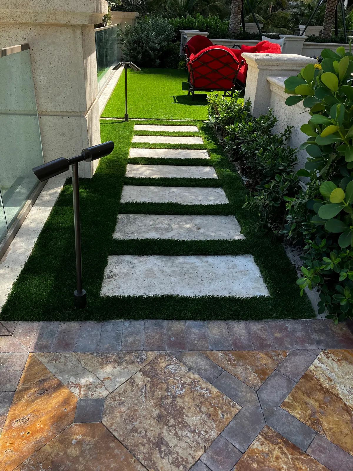 Stone steppers set in artificial turf with bronze path lights, leading from a travertine patio.
