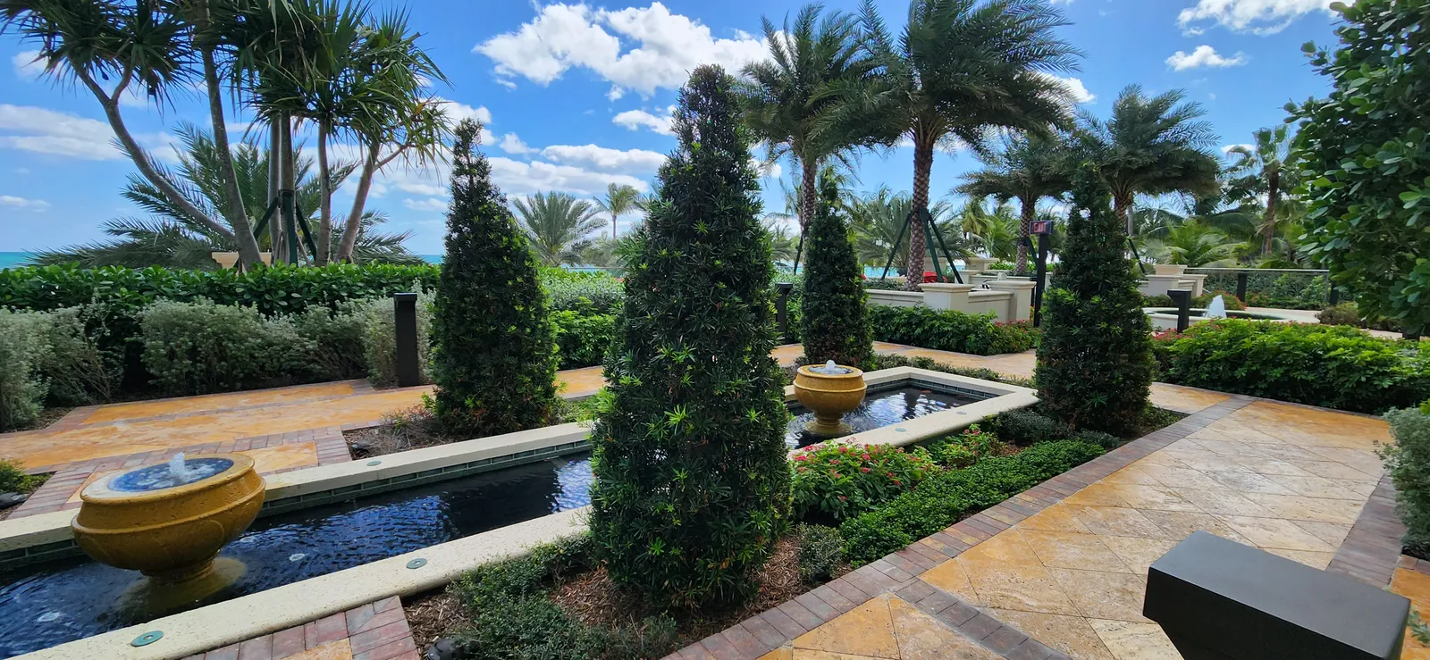 Formal oceanfront garden with cone topiaries, urn fountains, a reflecting pool and date palms.