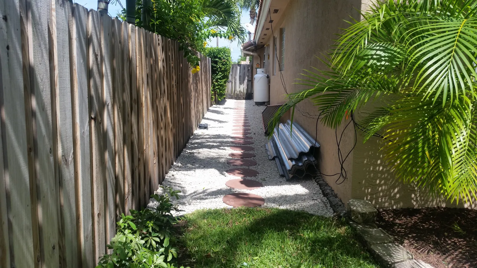 Side yard path of white gravel with round red stepping stones between a wood fence and the house.