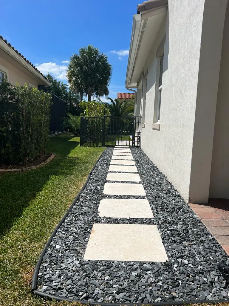 Square stone steppers in dark slate gravel along the side of a white stucco house.