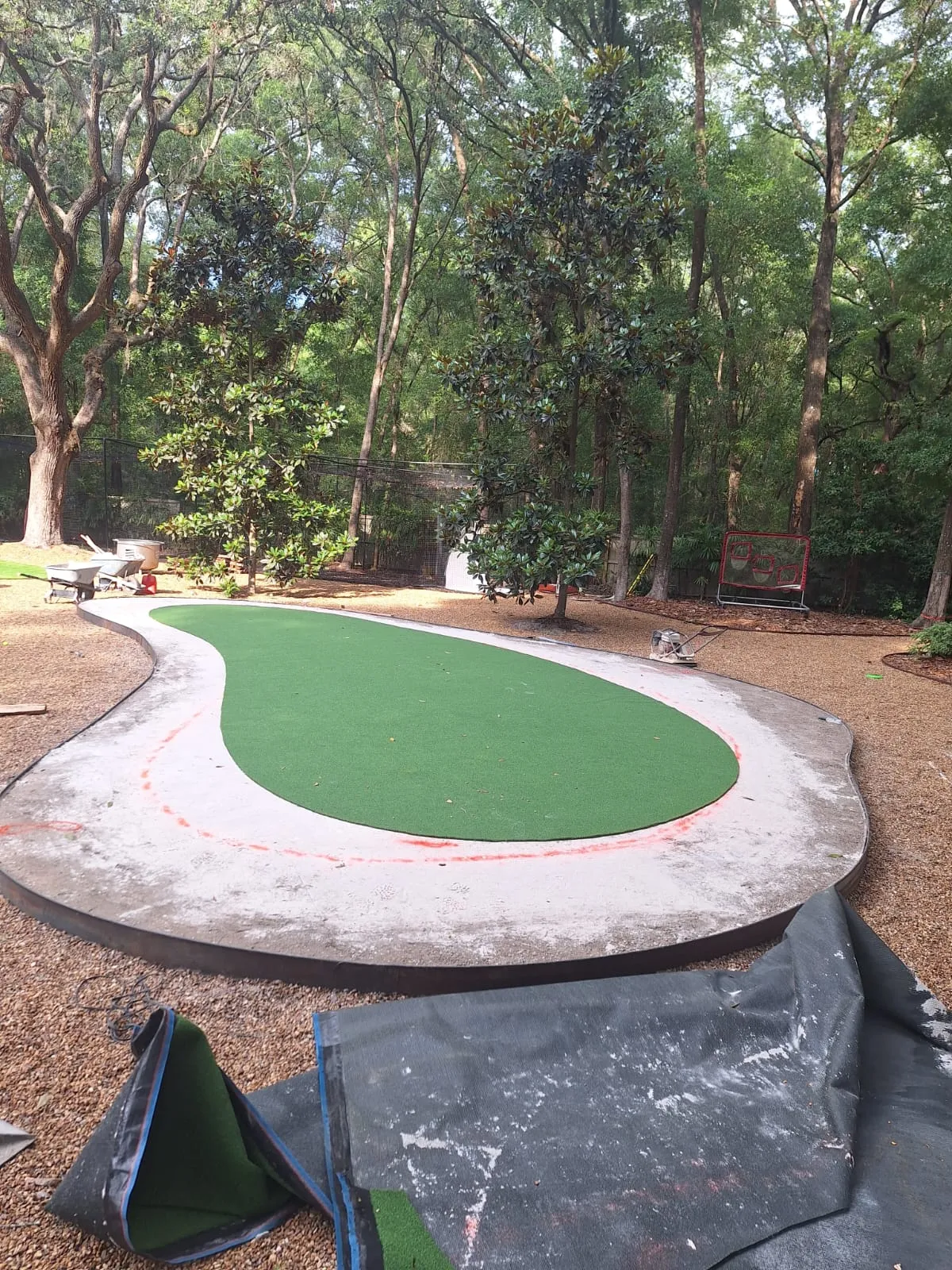 Putting surface turf cut and laid on a curved base with rolls of fringe turf waiting in front.