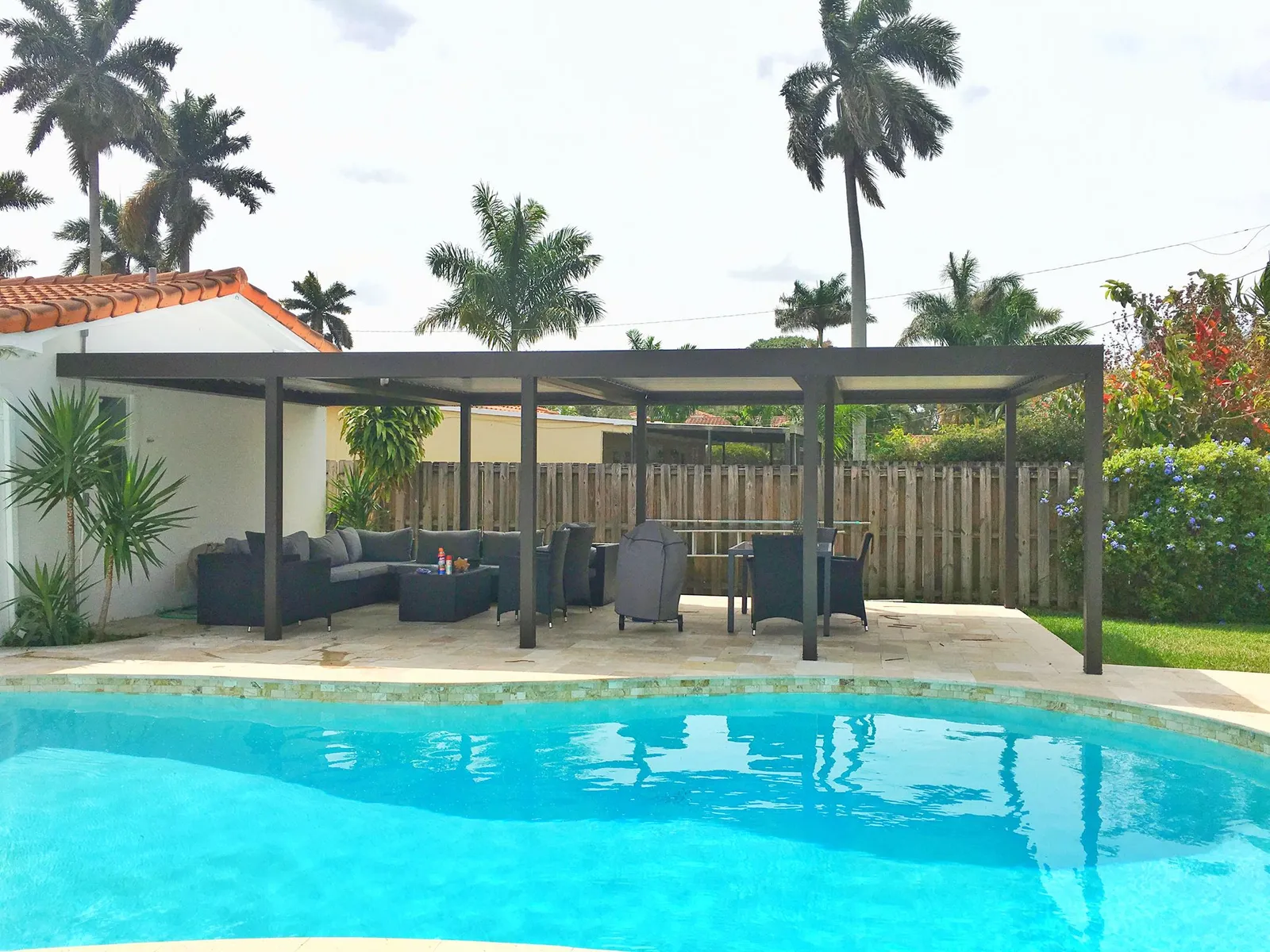 Bronze freestanding louvered pergola covering a lounge and dining area beside a freeform pool