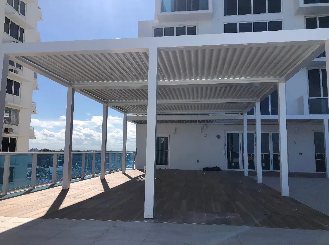 Finished white louvered pergola casting striped shade on a wood-look terrace.