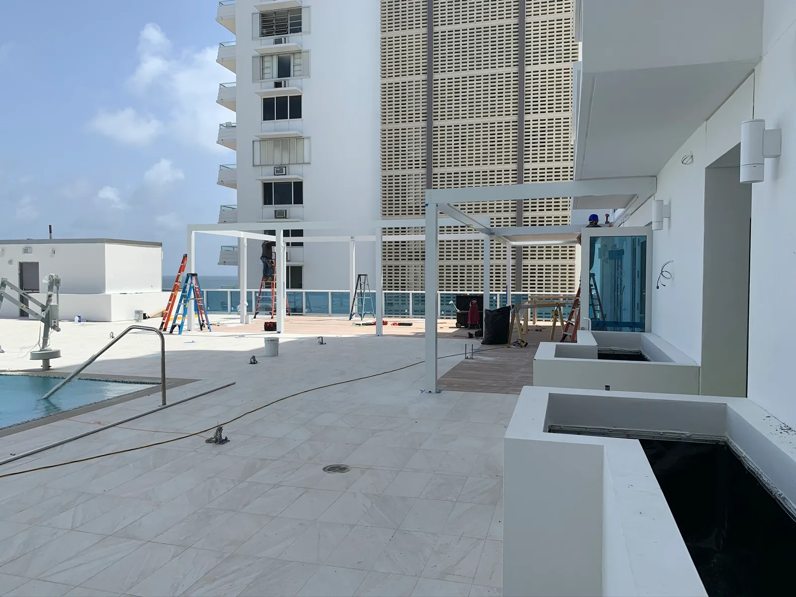 Rooftop terrace with white pergola frames under assembly and planters in the foreground.
