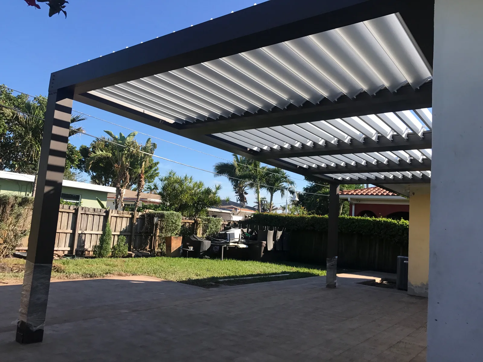 Bronze louvered pergola frame with white blades seen from below during installation in a backyard