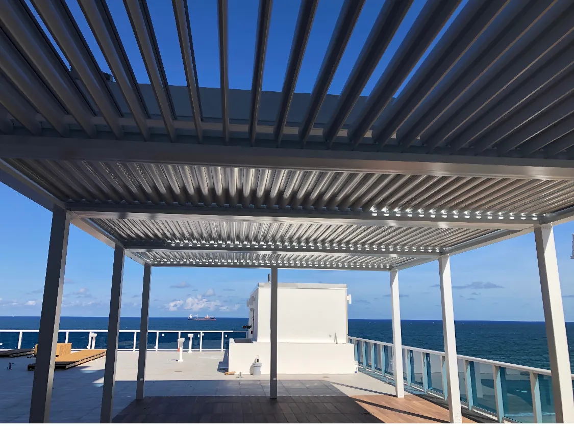 Looking up through open louvers of a white rooftop pergola toward the ocean.
