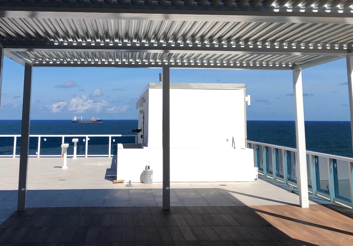 Open louvered pergola framing the ocean and a cargo ship from a rooftop terrace.