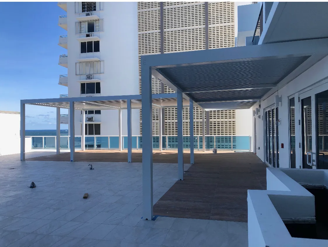 Row of finished white louvered pergolas along a condo terrace with ocean beyond.