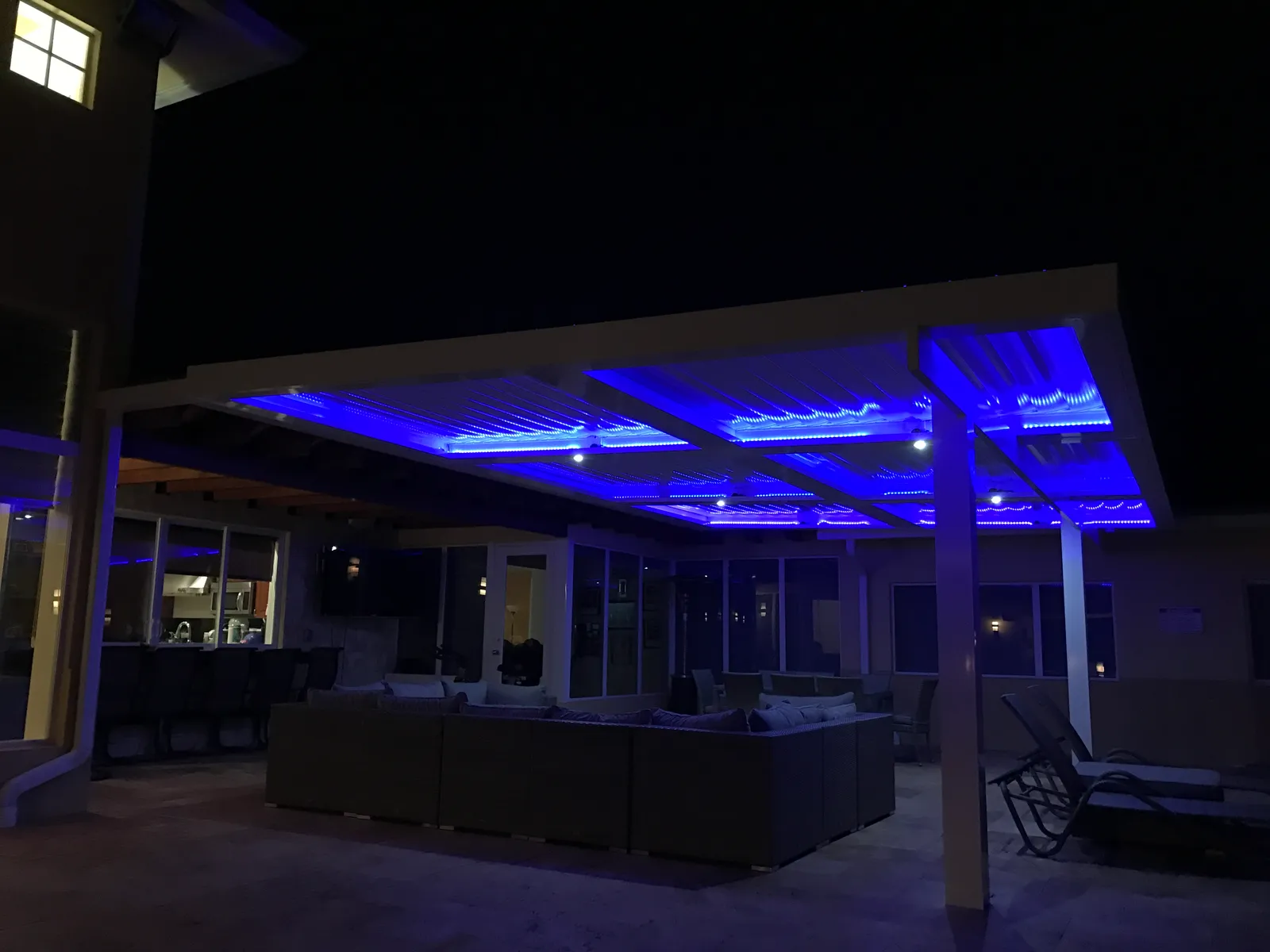 Louvered roof glowing with blue LED strips and spotlights over a dark patio at night