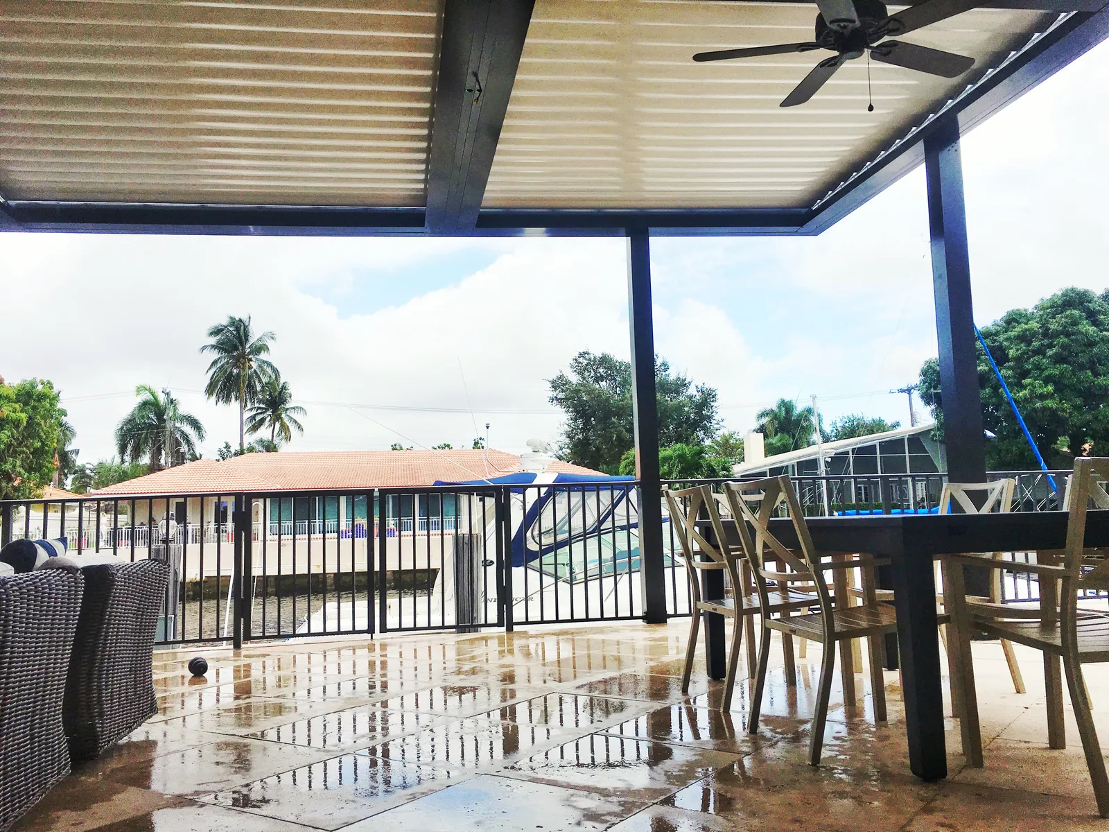 Closed louvered roof with ceiling fan over a wet travertine patio beside a canal dock