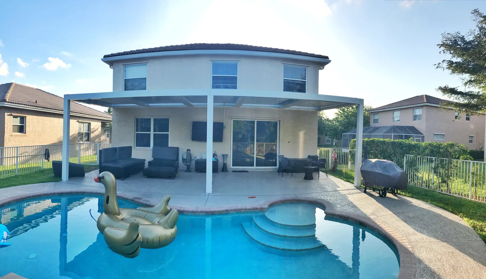 White attached louvered roof spanning the back of a two-story home behind a freeform pool