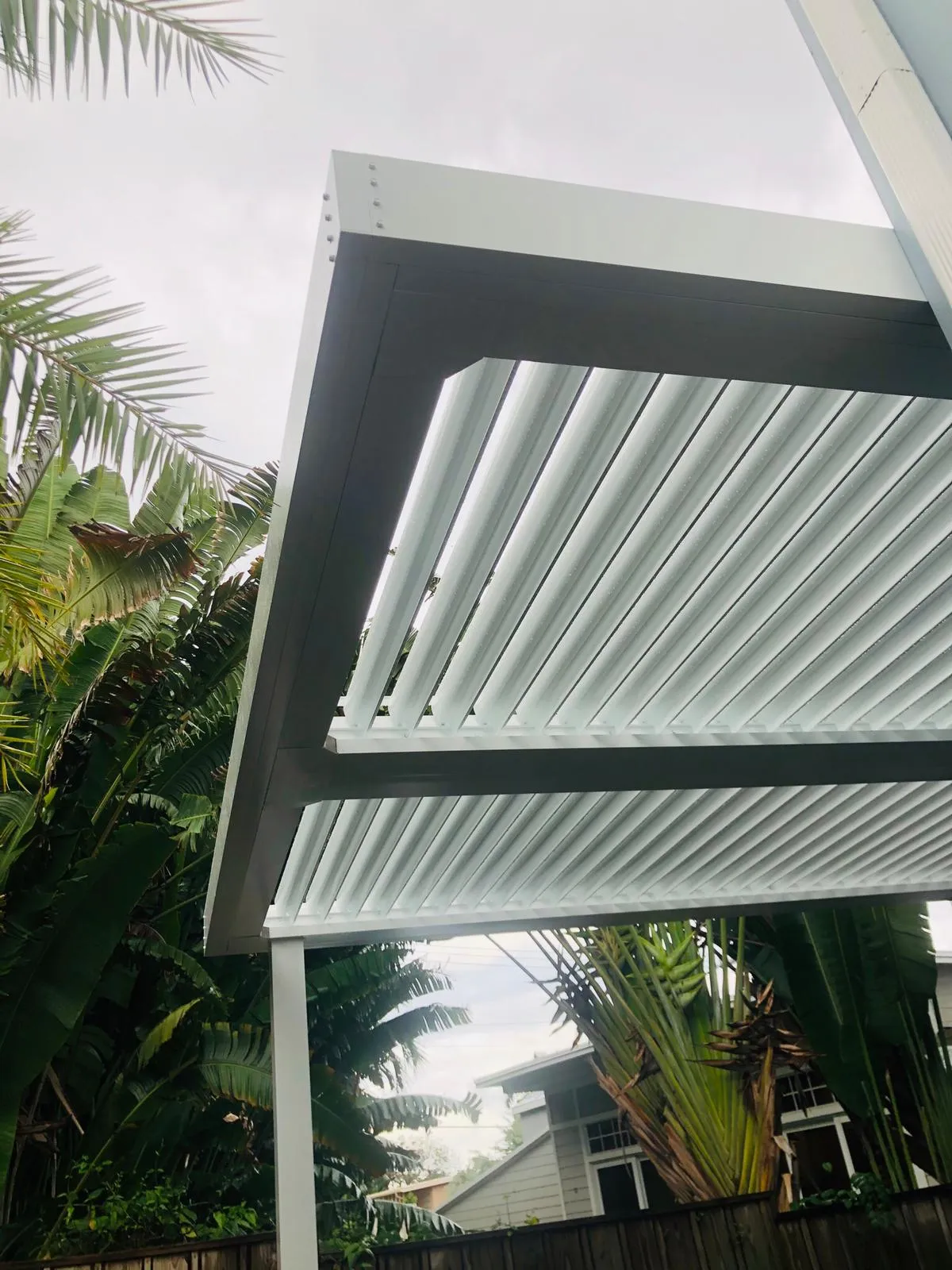 Corner of a white aluminum louvered roof showing the frame, rivets and angled blades