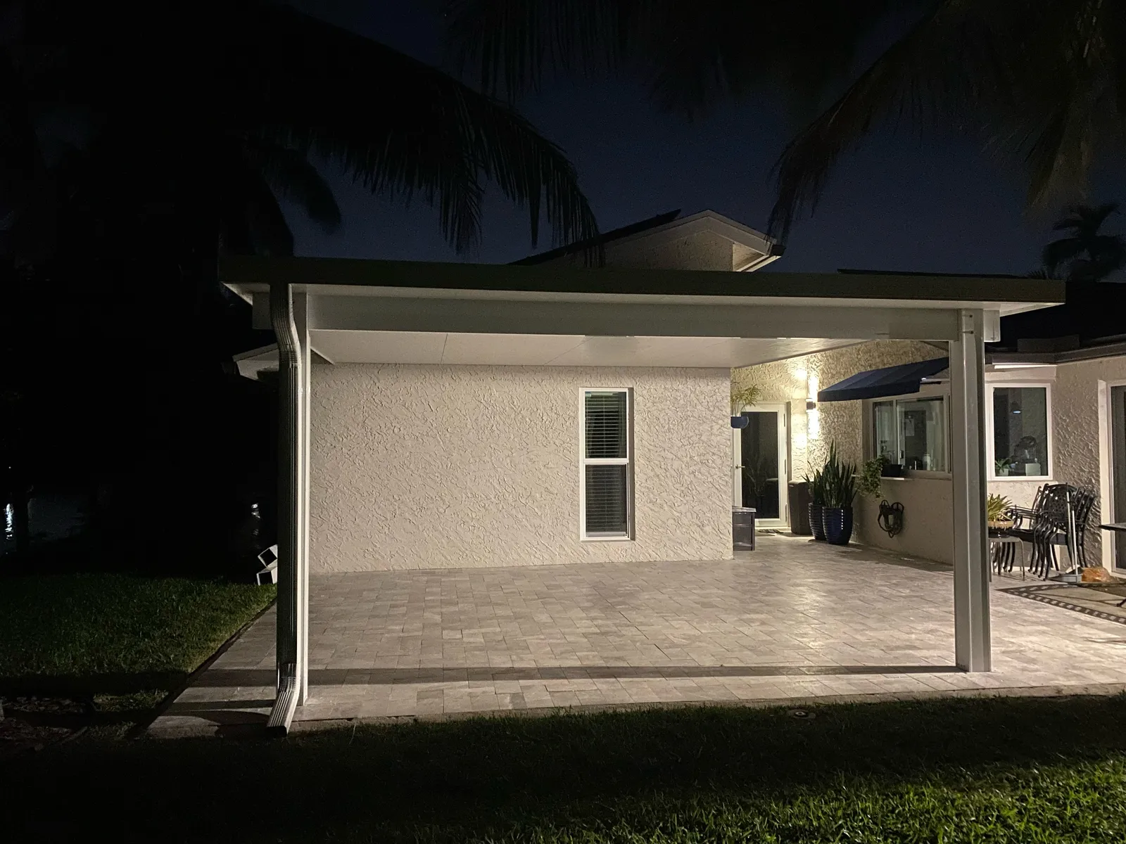 White insulated aluminum patio cover over a gray paver patio lit at night