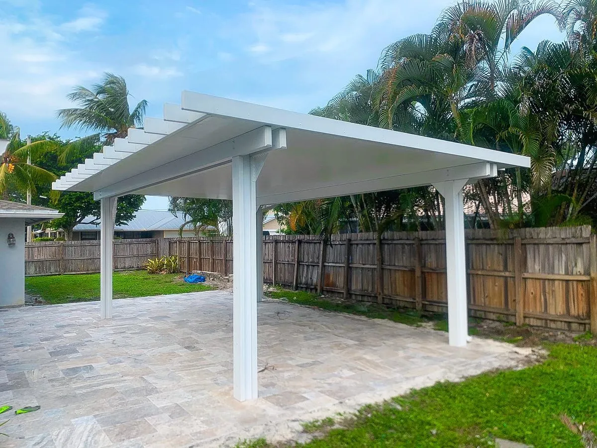 White freestanding insulated pergola with rafter tails on a travertine patio in a fenced backyard