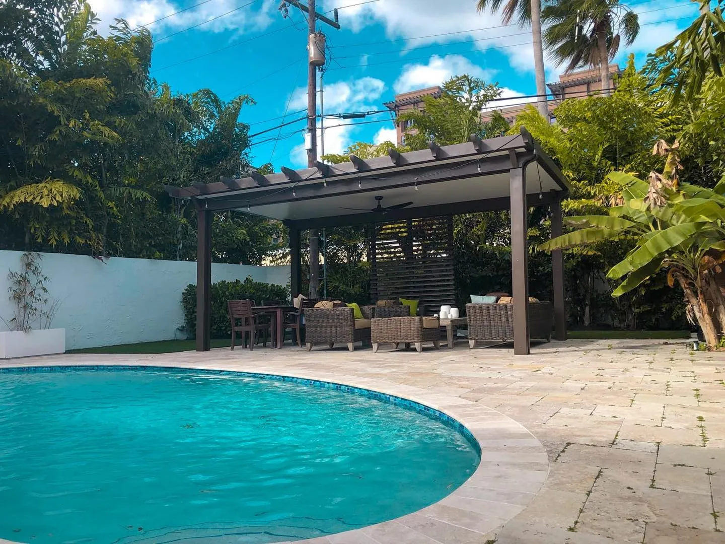 Freestanding bronze insulated pergola with slatted privacy screen and wicker seating beside a curved pool