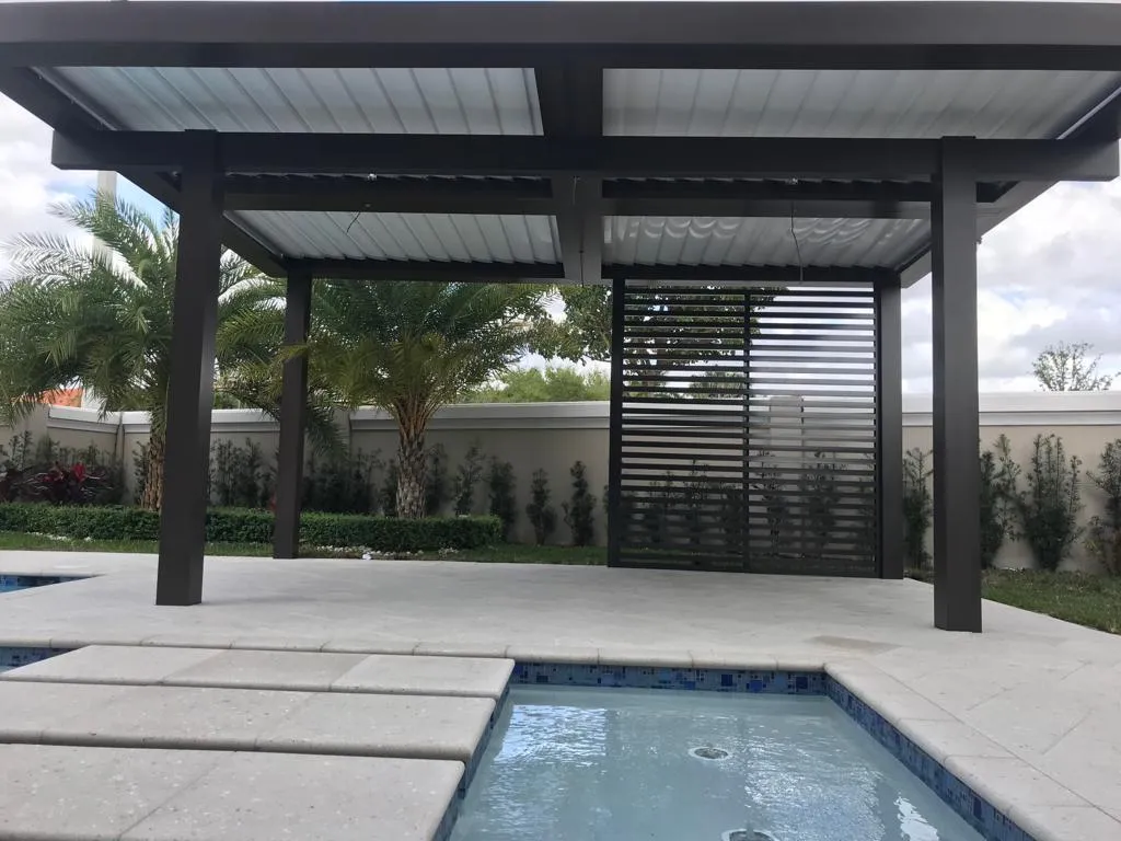 Freestanding dark aluminum patio cover with slat privacy screen beside a pool with stepping pads.
