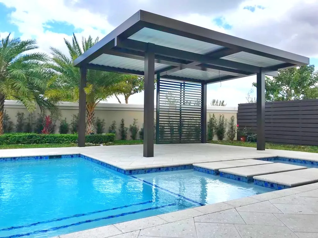 Freestanding dark aluminum patio cover with privacy screen on a pool deck with blue tile pool.