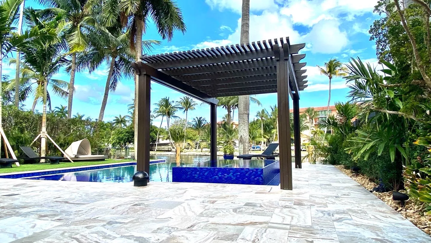 Dark bronze freestanding lattice pergola over a blue-tiled spa with canal and palms behind