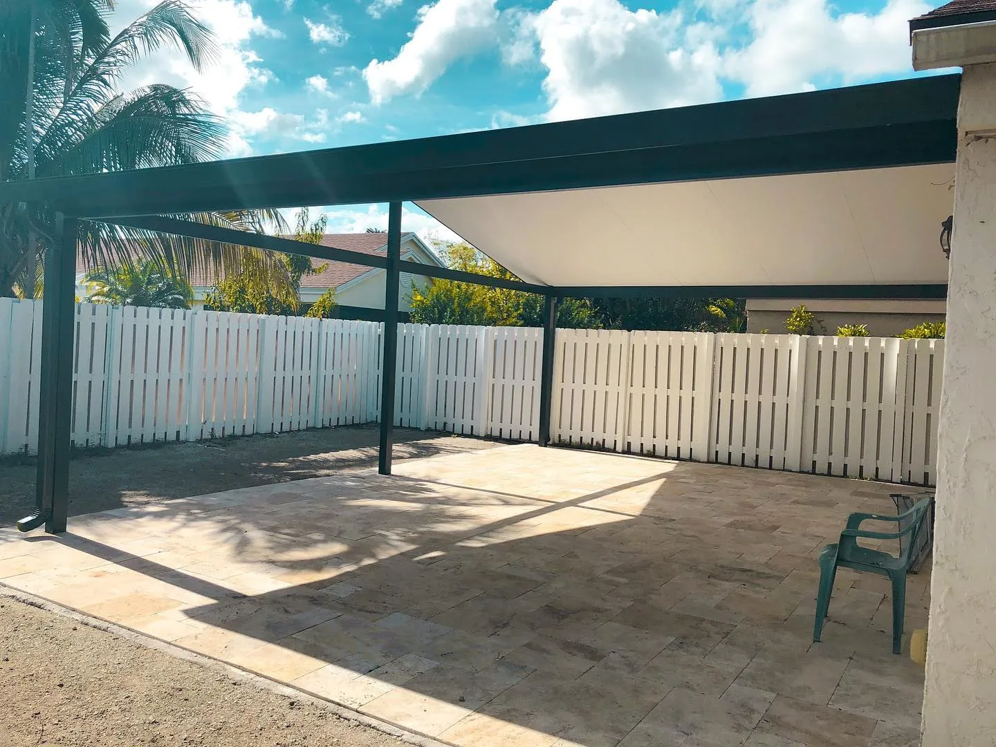 Side view under a dark-framed gable patio cover over a travertine patio with a white fence