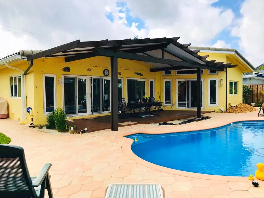 Dark-framed gable patio cover with rafter tails on a yellow house beside a kidney pool and hexagonal pavers