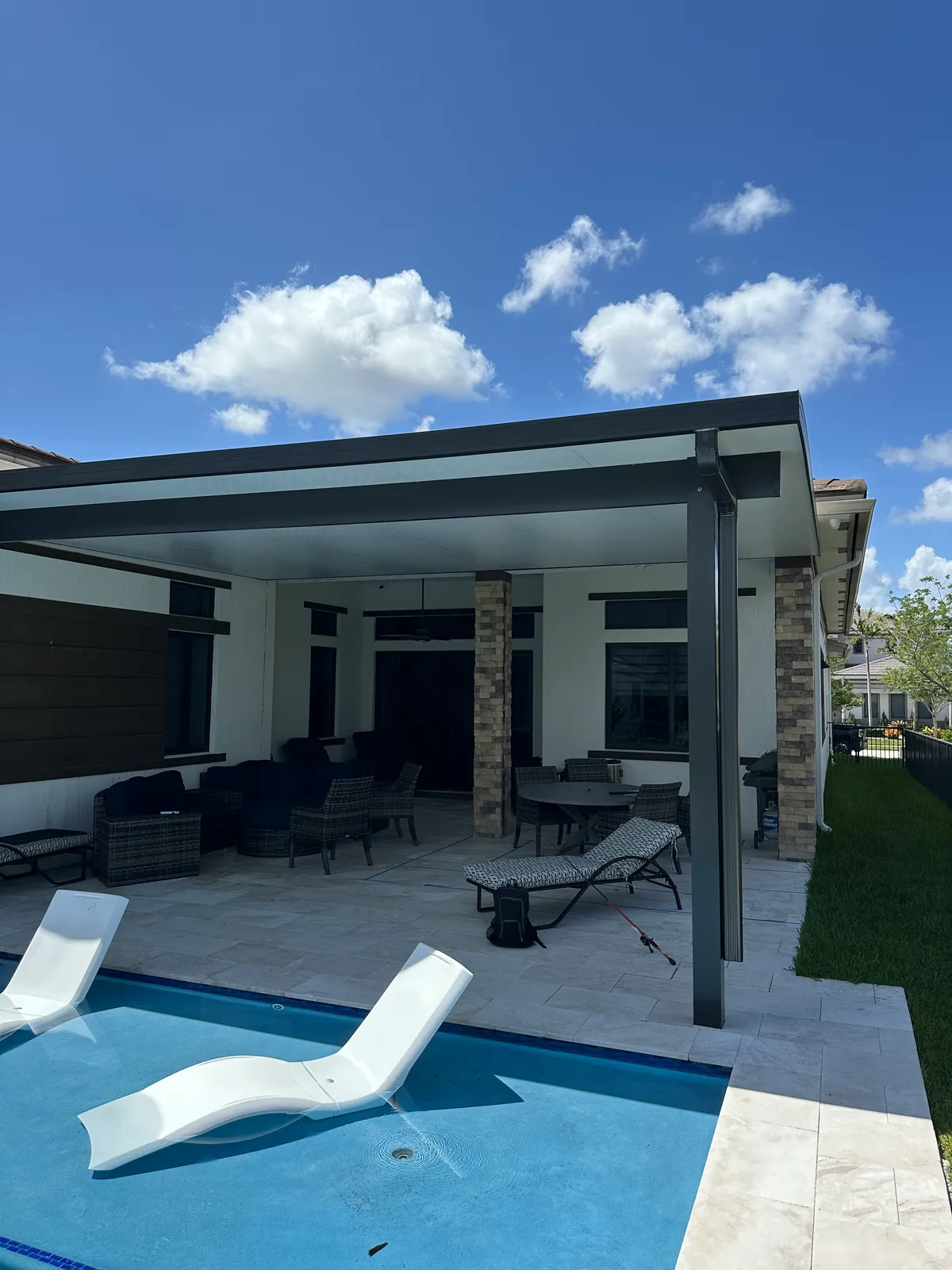 Dark bronze insulated aluminum patio cover over a travertine patio with wicker furniture beside a pool