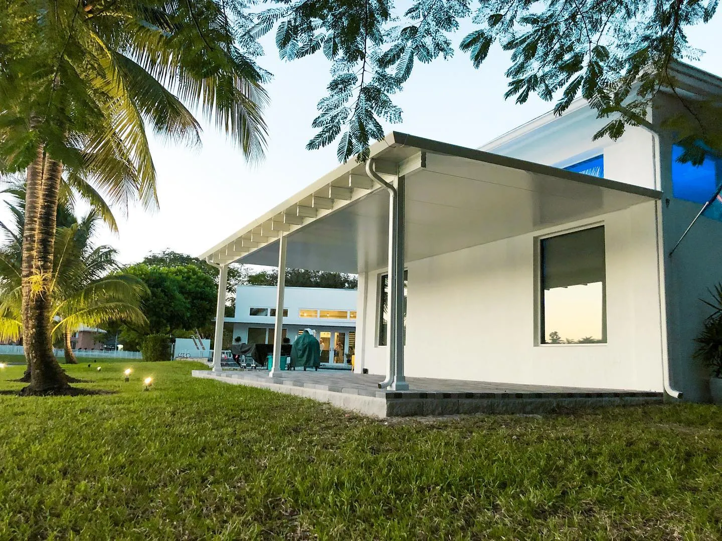 White insulated aluminum patio cover attached to a white house at dusk with palm trees and path lights